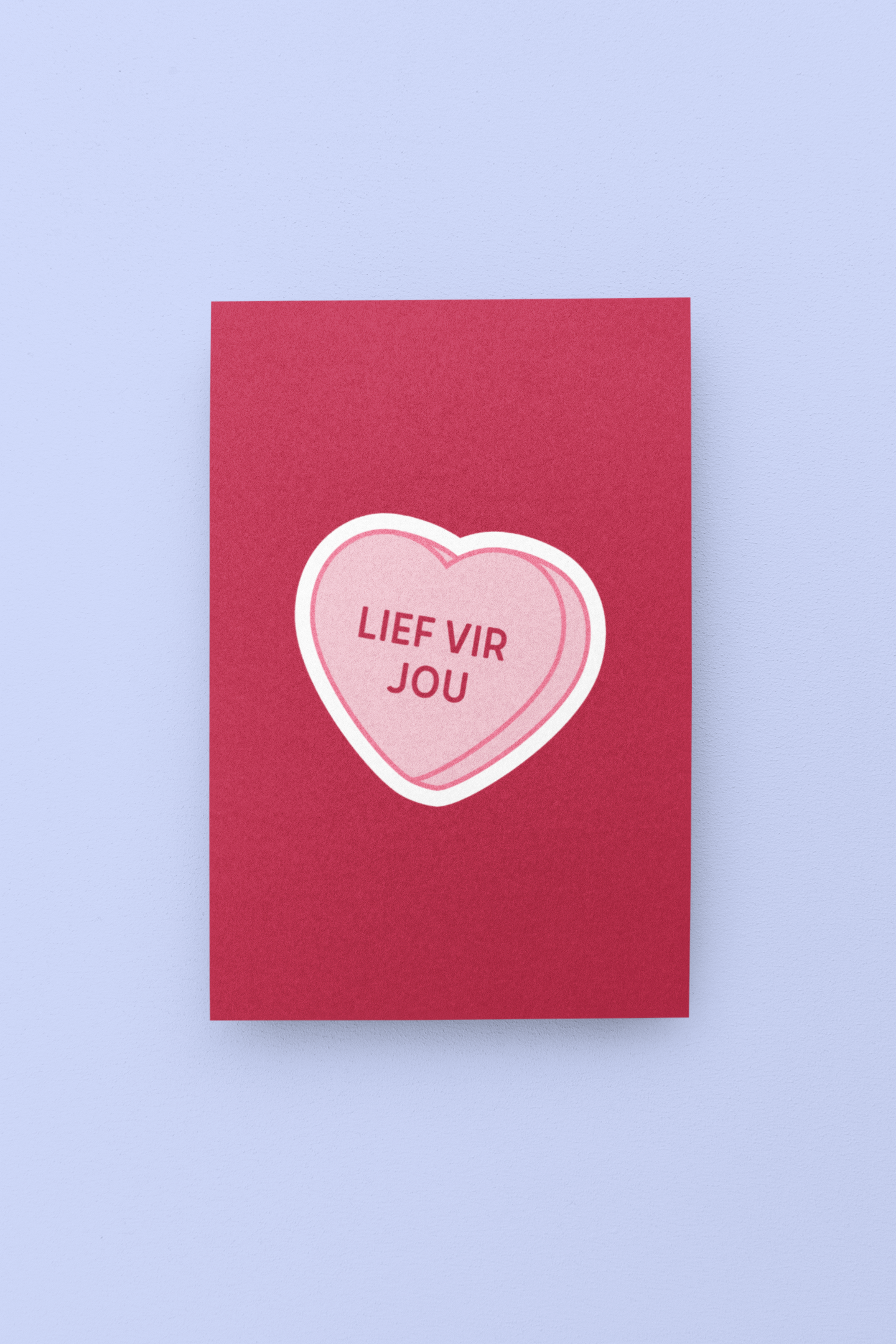 Red card with a pink heart-shaped candy on a light purple background