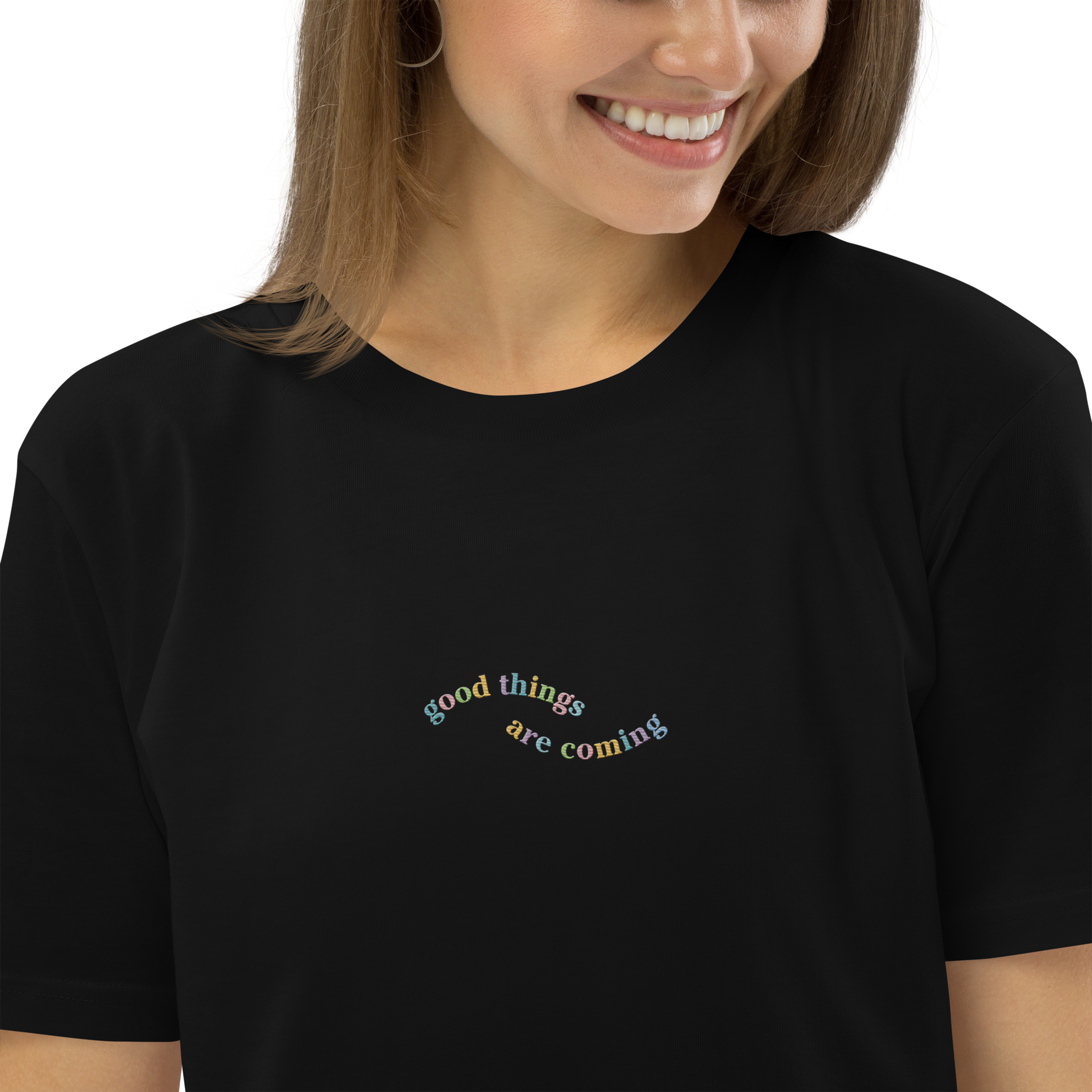 A smiling lady wearing a black t-shirt with the words 'good things are coming' embroidered on it.