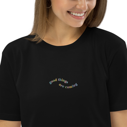 A smiling lady wearing a black t-shirt with the words 'good things are coming' embroidered on it.